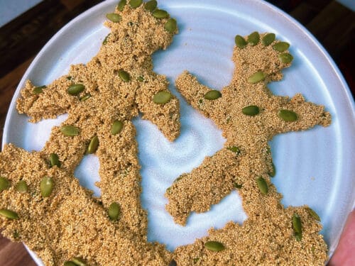 Four figure-shaped candies with granulated golden coating and green seed pieces on pale blue plate