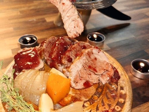 Sliced pork meat and sausage on wooden board with onion, herbs, and sauce