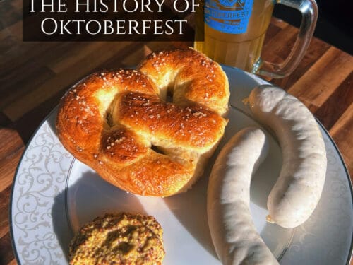 Salt pretzel, two sausages, and mustard on plate beside beer mug