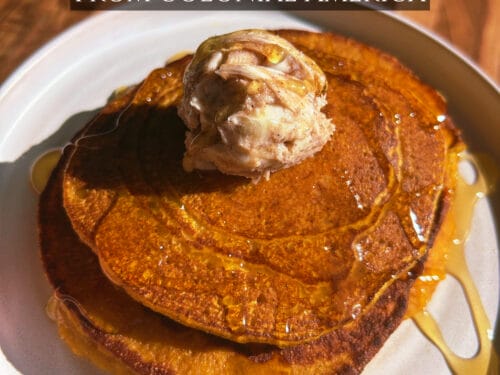 Two russet pancakes on a white plate topped with cinnamon cream and drizzled with amber syrup
