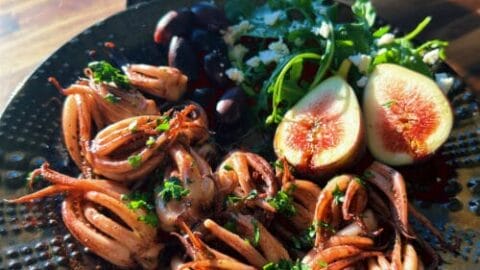 Roasted squid with fresh figs and green herbs on dark plate