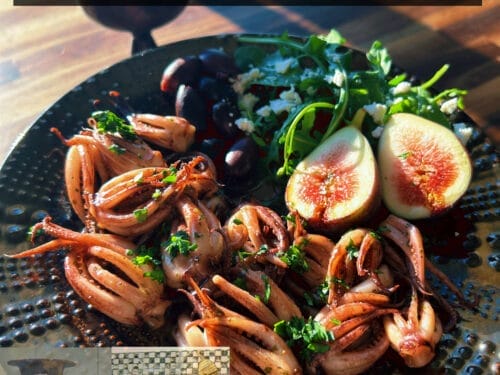 Roasted squid with fresh figs and green herbs on dark plate