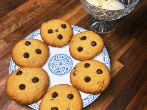 Chocolate chip cookies on blue-and-white plate, vanilla ice cream scoops in crystal bowl nearby