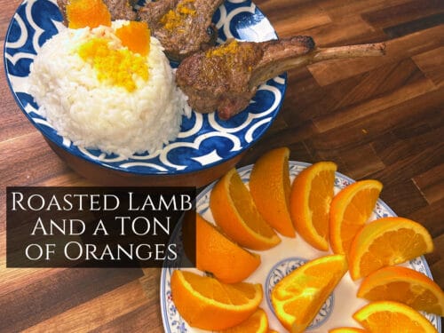 Roasted lamb chops and white rice with orange zest on blue-patterned plate, orange slices on separate plate