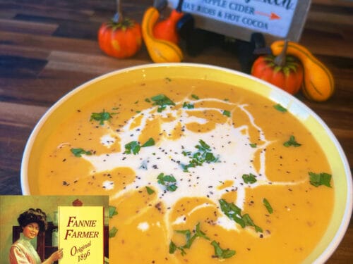 Butternut squash soup in white bowl with cream swirl, herbs, black pepper, small gourds nearby
