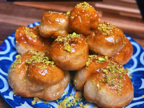 Glossy amber fried spheres dusted with crushed pistachios, arranged on blue and white patterned plate