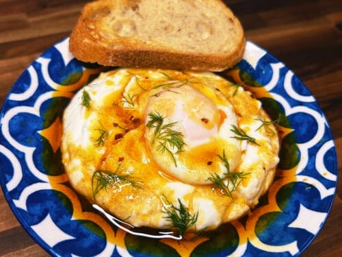 Poached eggs with dill and paprika oil on blue patterned plate with toasted bread