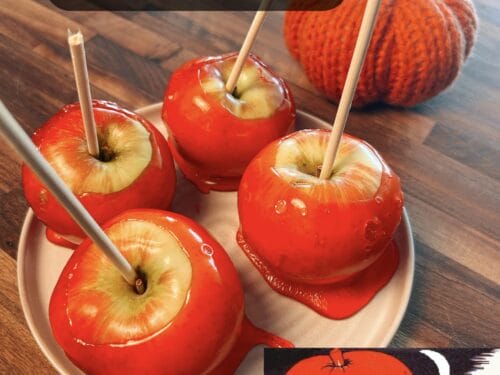 Four glossy red candied apples with wooden sticks on a pale plate