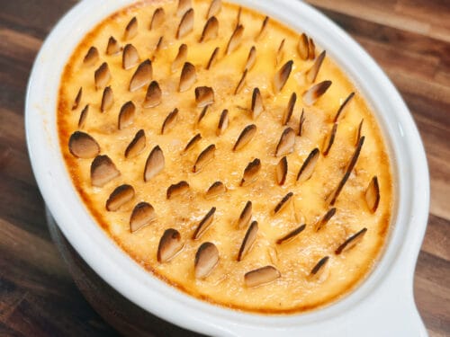 Baked custard in white oval dish with almond slices pressed across golden surface