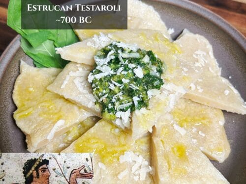 Pale rectangular pasta pieces drizzled with oil, topped with chopped green herbs and shaved white cheese, on a ceramic plate