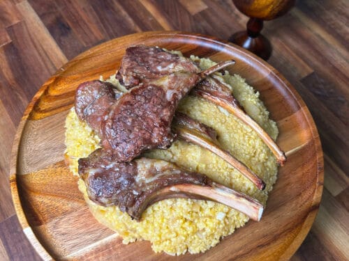 Seared lamb chops and yellow millet porridge on wooden plate with milk in wooden cup