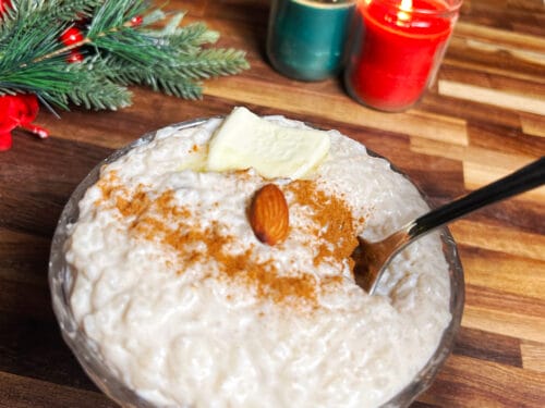 White pudding in glass bowl with cinnamon, almond, and butter, surrounded by evergreen sprigs and lit candles