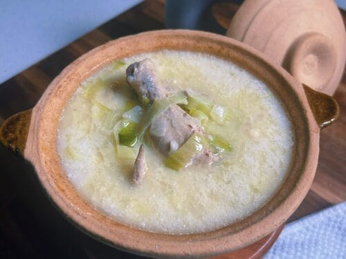 Pale soup with meat and leeks in earthenware bowl, blue vessel behind