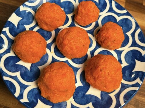 Seven rough-textured orange-red balls arranged on a blue and cream geometric ceramic plate