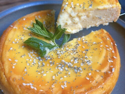 Creamy layered dessert on gray plate with golden glaze, sesame seeds, and mint leaf