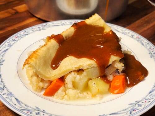 Pastry-topped pie slice with potatoes, parsnips, and carrots; gravy poured over plate