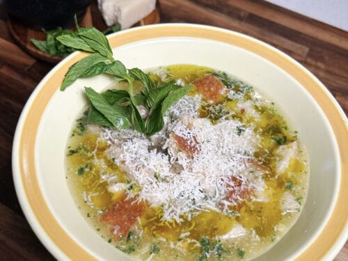 Yellowish soup with shredded cheese, herbs, and diced meat, garnished with fresh mint leaves