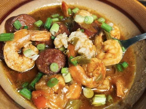 Bowl of stew with shrimp, sausage, okra, and green onions in dark broth
