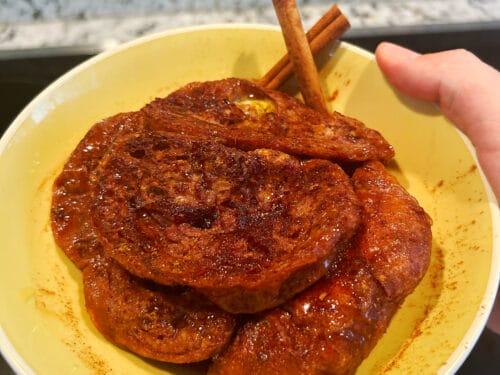 Golden-brown fried bread slices in yellow bowl with cinnamon sticks, held in hand