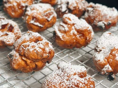 Multiple fried pastry balls heavily coated with powdered sugar arranged on a wire rack