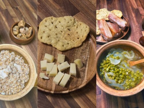 Wooden table with grain bowl, nuts, flatbread, cheese, cured meat, crackers, pea stew, and two dark goblets