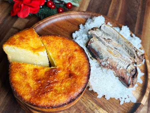 Golden-brown custard tart with fish fillets on bed of salt, wooden plate, festive candles and flowers
