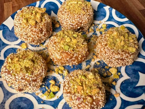 Seven round truffles with sesame seed coating and yellow-green crumbled topping on a blue and white geometric plate