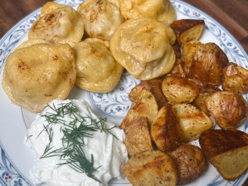 Porcelain plate with boiled dumplings, roasted potato wedges, and dollop of sour cream topped with fresh dill