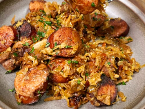 Spoonful of sausage pieces and shredded cabbage suspended above a plate of the same stew