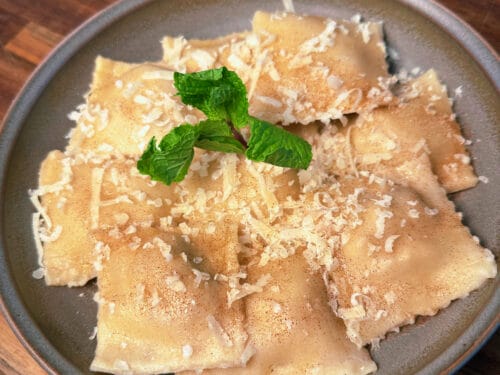 Folded pasta sheets dusted with grated cheese and cinnamon, garnished with fresh mint