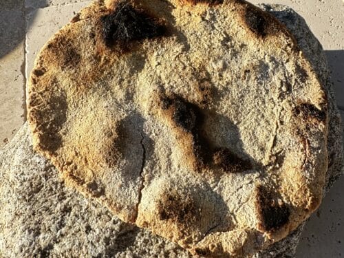 Round loaf with golden-brown crust and deep finger impressions on pale concrete surface