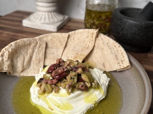 White cheese topped with chopped green and dark olives on gray plate with flatbread and olive oil