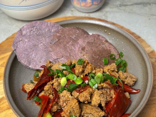 Gray ceramic plate with purple cornmeal flatbread, crumbled meat, red peppers, and green onions