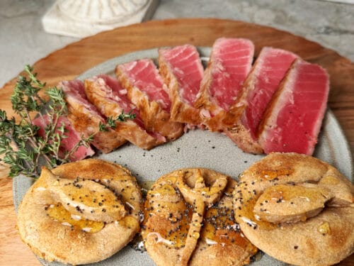 Raw tuna slices and round spelt cakes with black seeds on gray plate with herb sprig