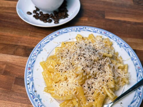 Bow-tie pasta topped with grated cheese and black pepper on blue-patterned plate, with black coffee and beans in white cup nearby