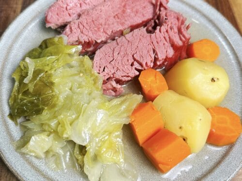Sliced pink meat, cooked cabbage, boiled potatoes, and carrot rounds on gray plate