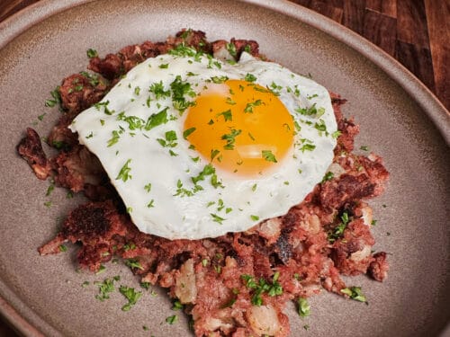 Chopped meat mixture with fried egg and herbs on tan ceramic plate