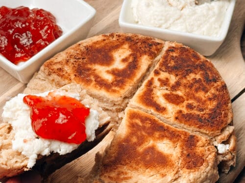 Sliced oatcake with white spread and red jam, accompanied by bowls of spread and jam