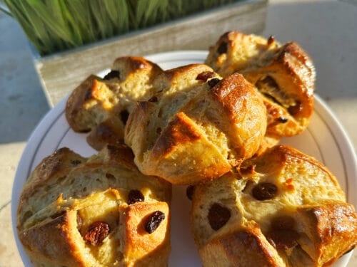 Golden-brown split buns studded with dark dried fruit on white plate in sunlight