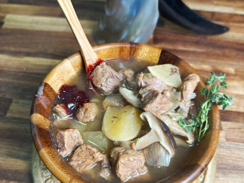 Meat stew with potatoes and mushrooms in carved wooden bowl with wooden spoon