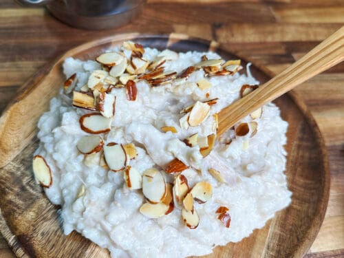 White creamy mound decorated with toasted almond slivers on wooden plate with spoon