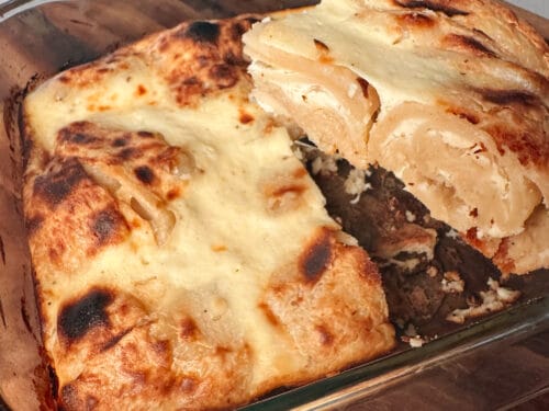 Pastry in glass baking dish with one slice removed, exposing dark filling and creamy interior layers