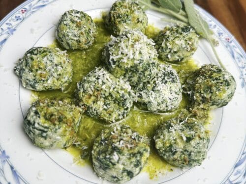 Herb-coated dumplings in olive oil on white plate with fresh sage leaves