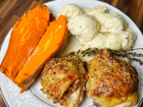 White plate with roasted poultry, orange pepper halves, creamed potatoes, and fresh herb garnish on wooden table
