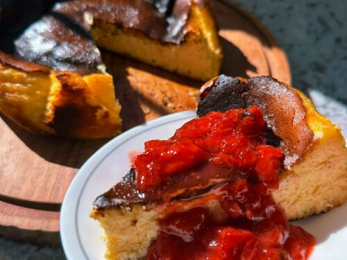 Sliced round dessert with dark charred top, creamy interior, and bright red sauce on white plate