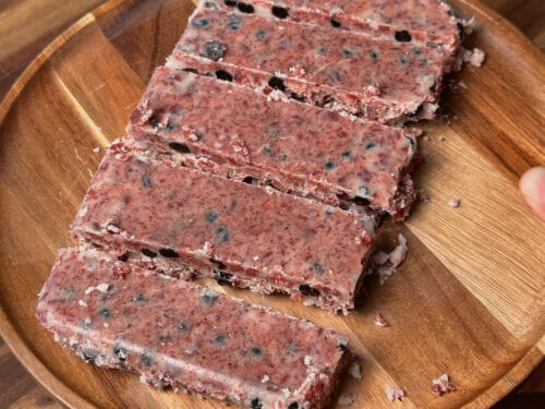 Rectangular meat bars with visible dark specks arranged on a round wooden plate