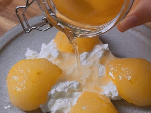 Golden syrup poured from glass jar onto peeled pears and whipped cream on plate