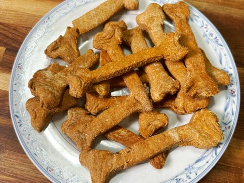 Golden-brown bone-shaped biscuits arranged on white plate with blue floral rim